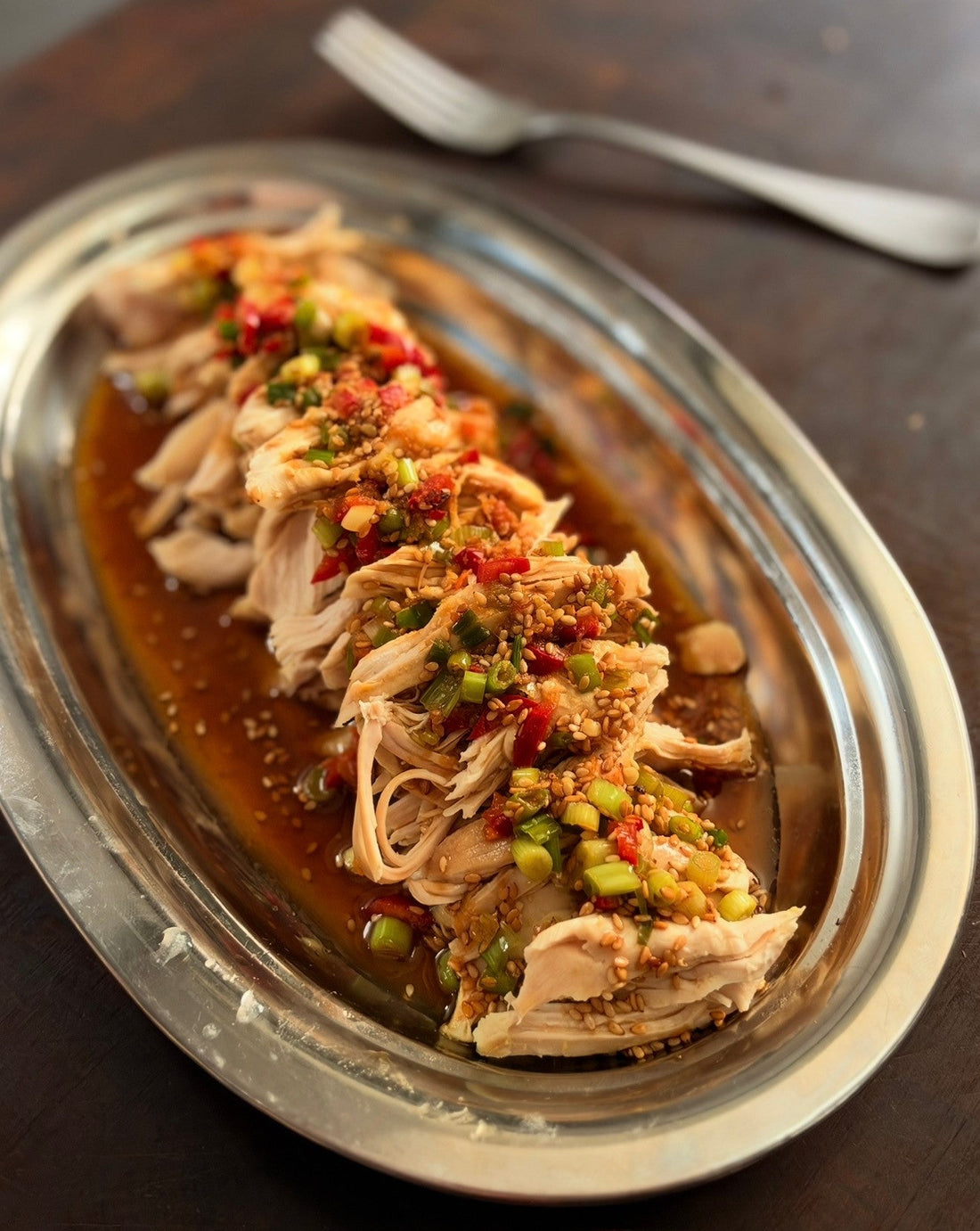 Shredded chili-scallion chicken with red chili, scallions and sesame seeds on a silver serving platter