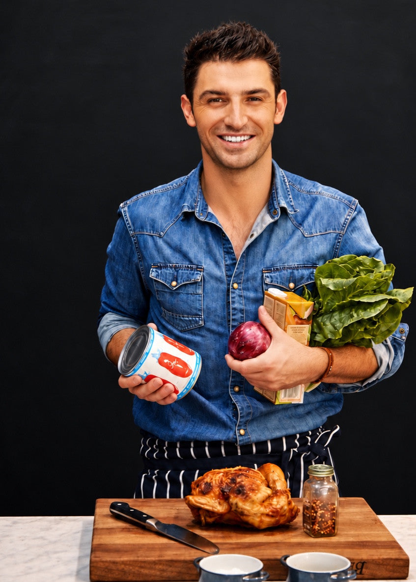 Chef Stu in a denim shirt holding fresh ingredients behind a roast chicken