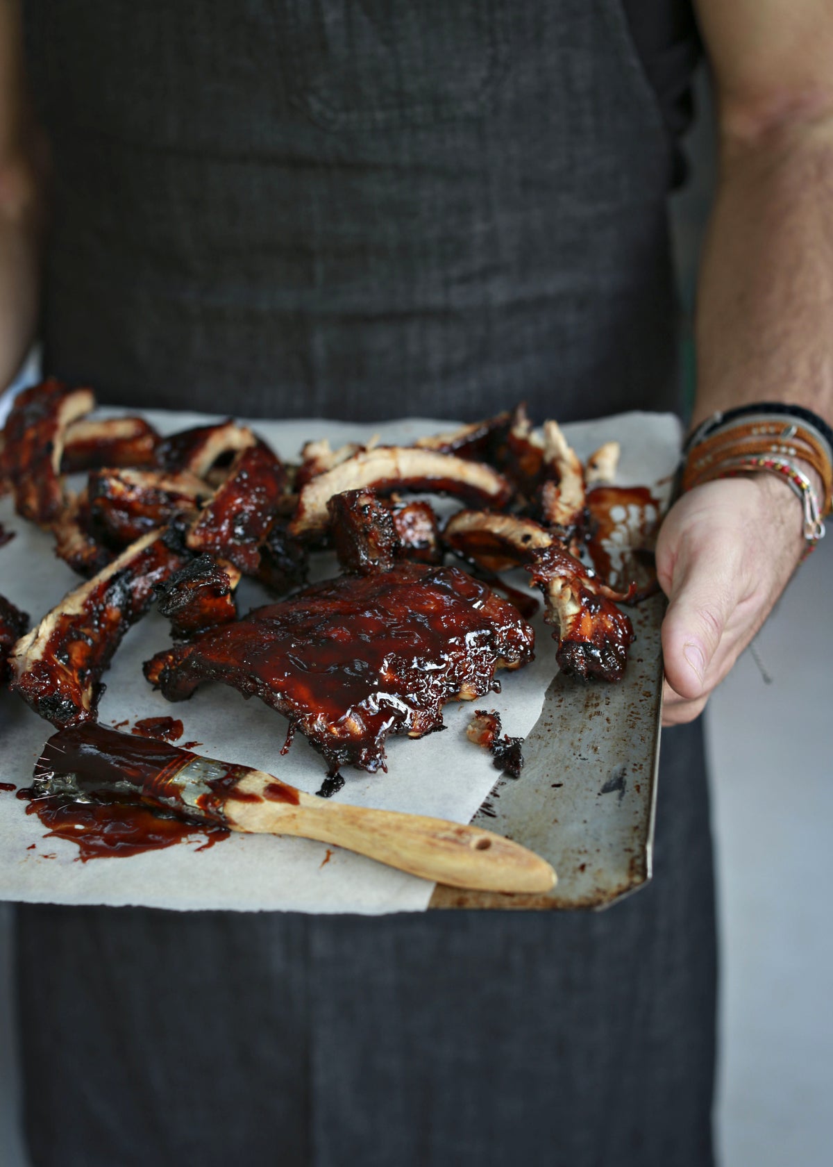 A tray of glossy barbecue ribs held by a cook, with a basting brush
