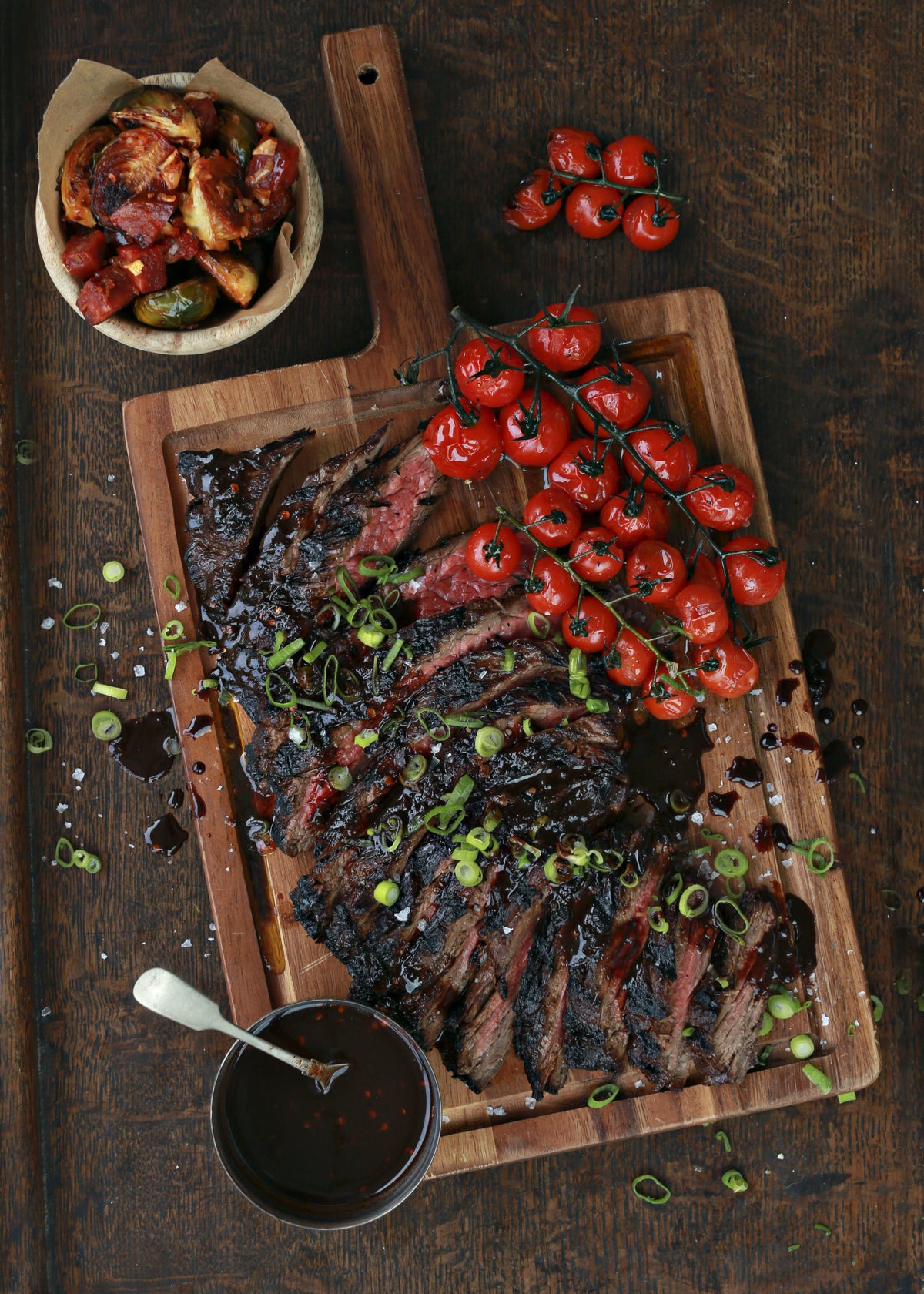 Sliced grilled steak with cherry tomatoes and spring onions on a wooden board