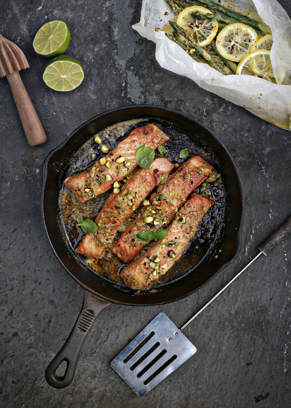 Salmon with basil and pistachios in a skillet beside lemon-topped asparagus