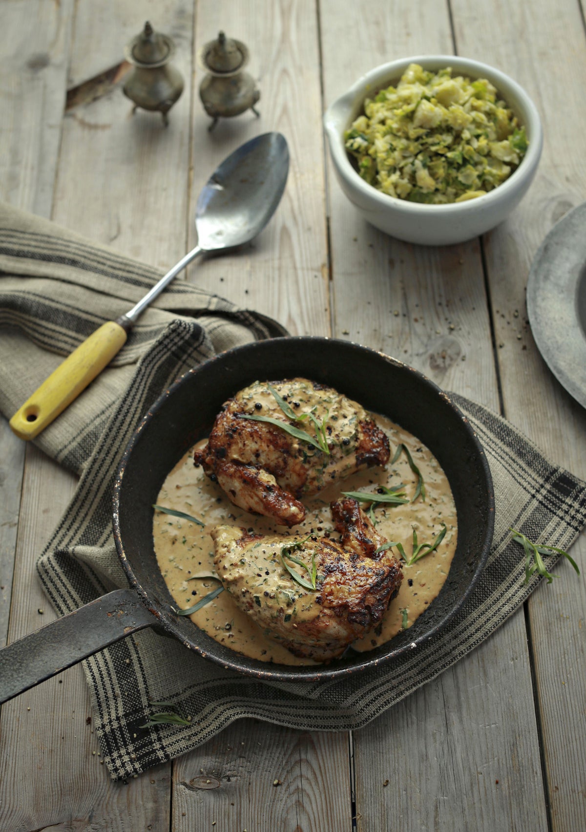Golden chicken in a skillet with creamy herb sauce and a bowl of Brussels sprouts