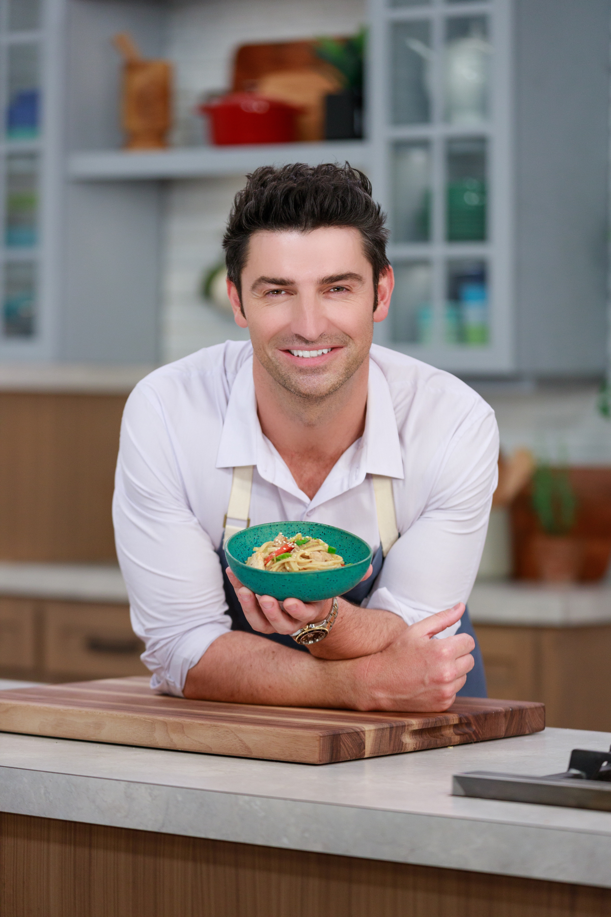 Chef Stuart holding a turquoise bowl of pasta in a bright kitchen.